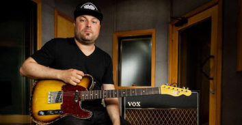 seated man holding electric guitar beside VOX amplifier