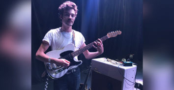 male musician holding electric guitar beside VOX amplifier