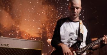artist, Joff Oddie, in concert playing electric guitar beside VOX amplifier