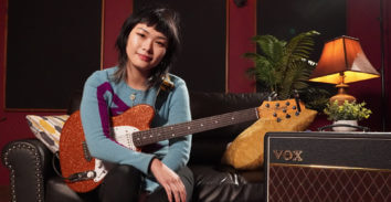 woman with electric guitar seated on leather sofa beside VOX amplifier